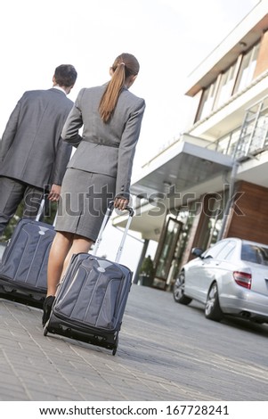 Back view of business couple walking with luggage on driveway