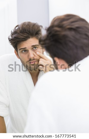 Reflection of ill man examining eyes in mirror