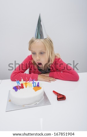 Surprised girl looking at birthday cake on table in house