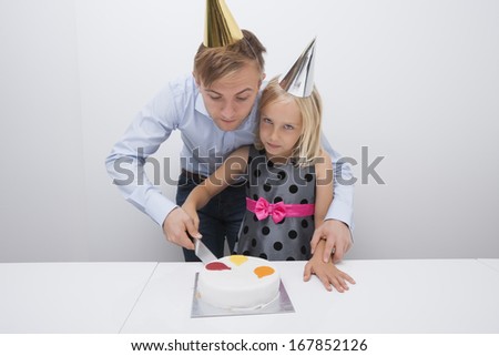 Father and daughter cutting birthday cake at table