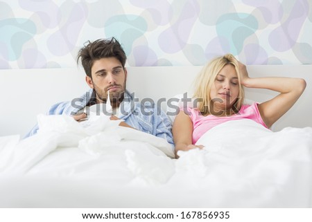 Frustrated sick couple lying in bed at home