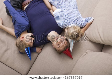 High angle view of father and children with artificial mustache and party hat sleeping on sofa bed