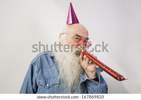 Portrait of senior man wearing party hat while blowing horn against gray background