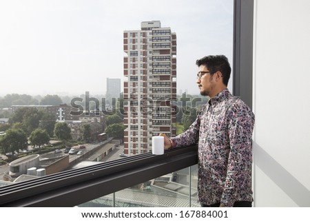 Young man with coffee mug looking out through window at home