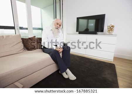 Sad senior man sitting on sofa in living room