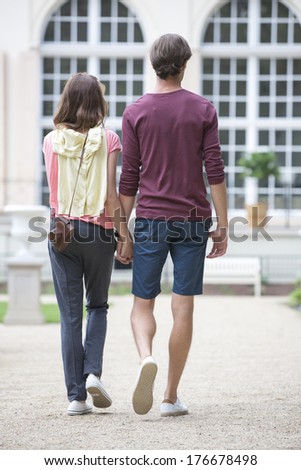 Full-length rear view of young couple walking against building
