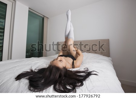 Full length of sexy young woman with legs raised in bed
