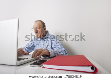 Senior businessman using laptop with book binder and cell phone on office desk