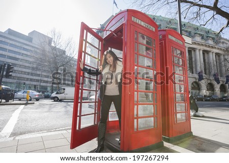 Portrait of happy young woman opening door of telephone booth at London; England; UK