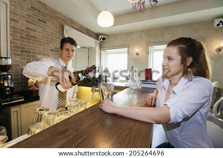 Bartender pouring wine for female customer at restaurant counter
