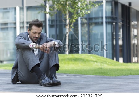 Full length of sad businessman sitting on path outside office