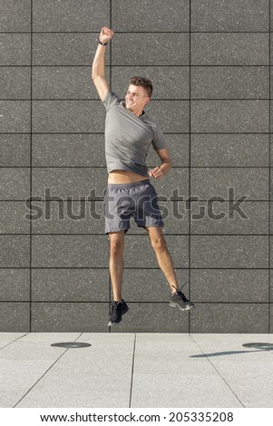 Full length of excited runner jumping against tiled wall