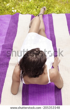 Young woman leaning on elbows while lying on picnic blanket in park