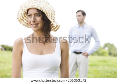 Thoughtful young woman smiling while man standing in background at park