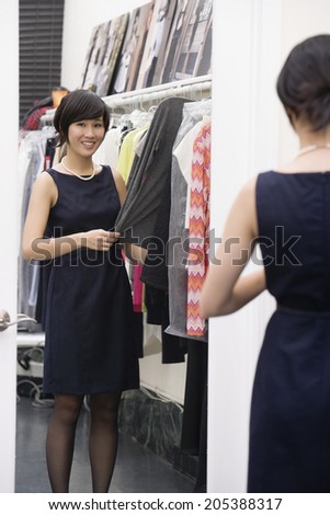 Young woman standing by the clothing rack in front of mirror