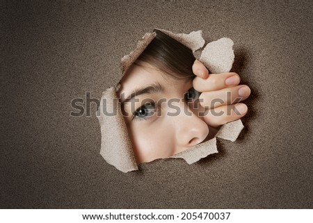 Portrait of a young Middle eastern woman peeking from ripped white paper hole
