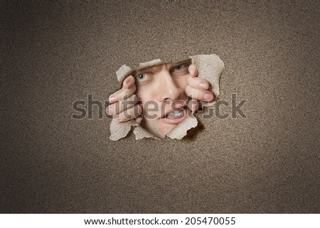 Portrait of a aggressive mid adult man peeking from ripped white paper hole