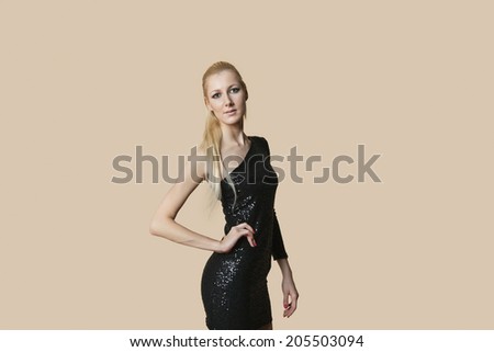 Portrait of a beautiful blond woman wearing cocktail dress with hands on hips over colored background