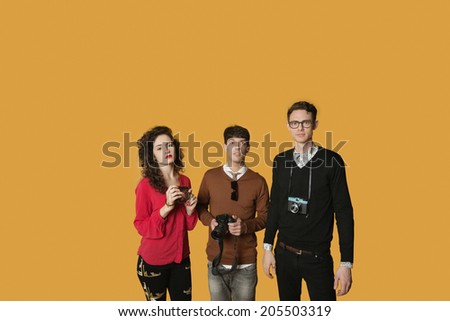 Portrait of friends standing together with cameras over colored background
