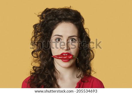 Portrait of a young woman with red chili pepper in mouth over colored background