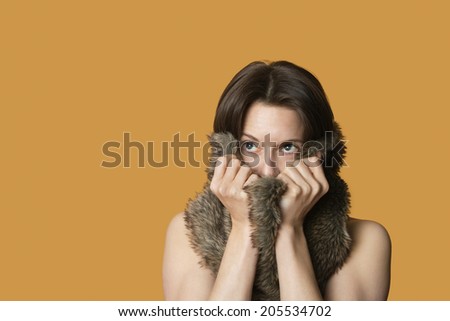 Close-up of woman with fur on face looking away over colored background