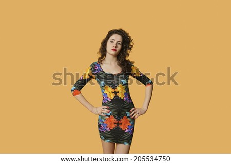 Portrait of a confident young woman posing with hands on hips over colored background