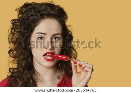 Portrait of a young woman biting red chili pepper over colored background