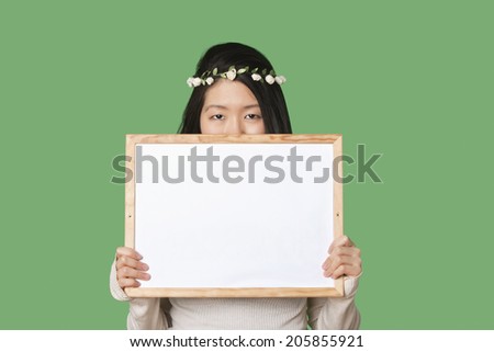 Portrait of a young woman hiding her face with a blank whiteboard over green background