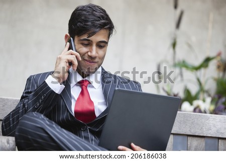 An Indian businessman using tablet PC while communicating on cell phone