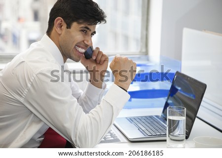 Excited businessman using cell phone at office desk
