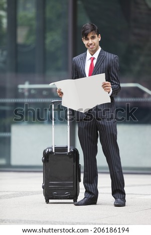 Young Indian businessman with luggage bag reading paper