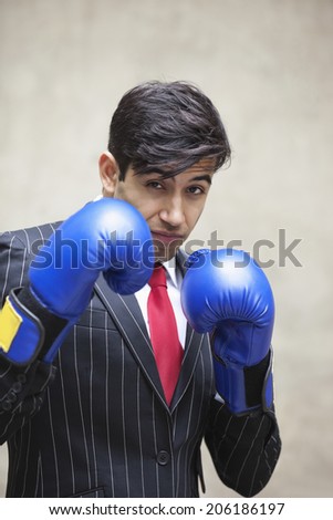 Portrait of an Indian businessman wearing blue boxing gloves against gray background