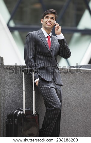 Young Indian businessman communicating on cell phone while standing next to luggage bag