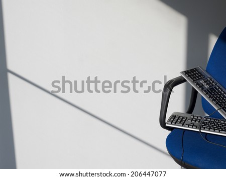 Closeup of two computer keyboards on office chair against wall