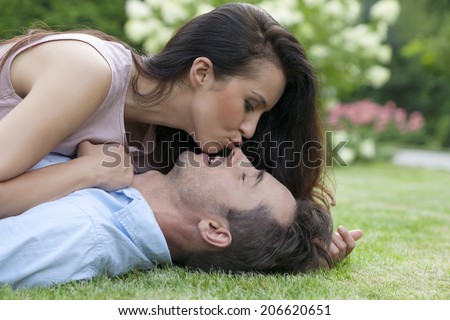 Side view of young woman kissing man while lying in park