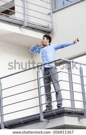 Full length of young businessman stretching at hotel balcony