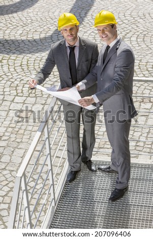 Full length portrait of young businessmen with blueprint on stairway