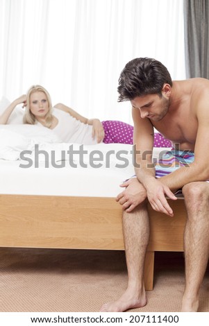 Sad young man on bed with woman in background at hotel room