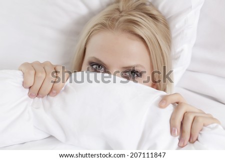 Close-up portrait of young woman covering face with bed sheet