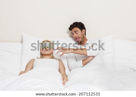 Angry young man teasing sleeping woman in bed