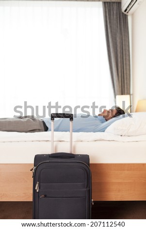 Side view of young businessman sleeping in bed by luggage at hotel