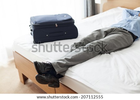 Low section of young businessman sleeping beside suitcase in hotel room