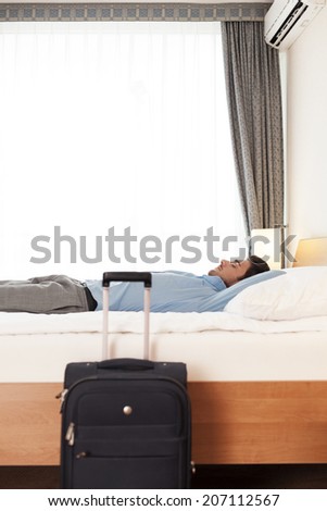 Side view of young businessman sleeping in bed by luggage at hotel room