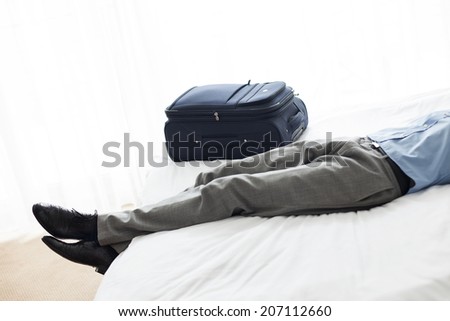 Low section of businessman sleeping beside luggage in hotel room