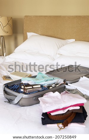 Closeup of stacks of folded clothes and packed suitcase on bed