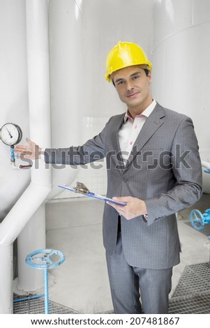 Portrait of confident young male manager with clipboard showing machine in industry