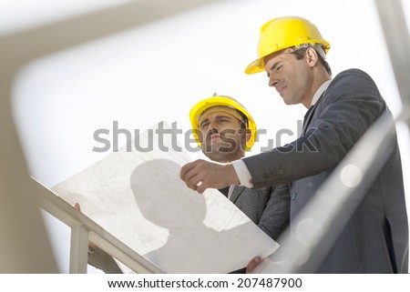 Low angle view of young businessmen holding blueprint against clear sky