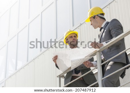 Full length of young businessmen discussing over blueprint on stairway