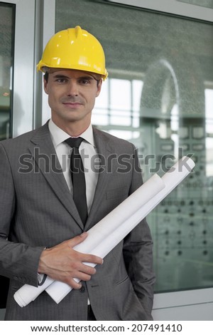 Portrait of confident young male architect holding blueprints in industry