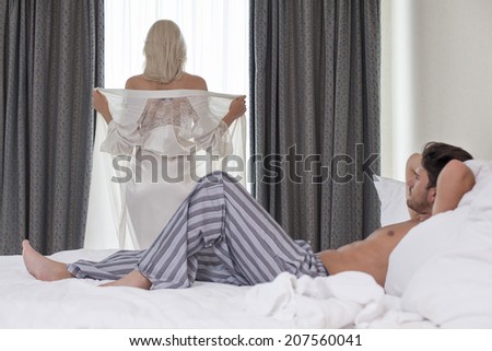 Full length of young man looking at woman removing robe at window